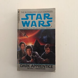May include: A paperback book titled "Star Wars: Dark Apprentice" by Kevin J. Anderson. The cover displays the Star Wars logo in blue, with a dramatic illustration of characters and a dark, space-themed background. It's part of the Jedi Academy Trilogy.