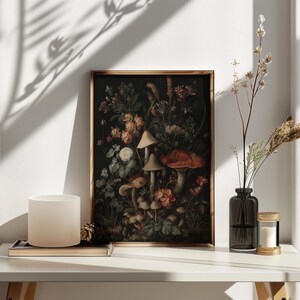 May include: A framed botanical print with a dark backdrop, showcasing mushrooms and flowers in red, orange, and white hues. The artwork is in a gold frame, displayed on a white surface.