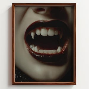 Puede incluir: Una impresión enmarcada que presenta un primer plano de una boca con lápiz labial rojo oscuro y colmillos blancos y afilados. La boca abierta revela dientes blancos y un interior oscuro. El marco es de color marrón oscuro.