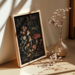 May include: A framed art print with a botanical illustration of mushrooms and flowers in red, white, and green hues. The print is displayed beside a vase of dried flowers, creating a natural, earthy aesthetic.