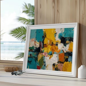 May include: A framed abstract painting with a white border. The artwork features bold brushstrokes in shades of yellow, teal, orange, white, and black. The painting is displayed on a white surface near a window with a view of the ocean.