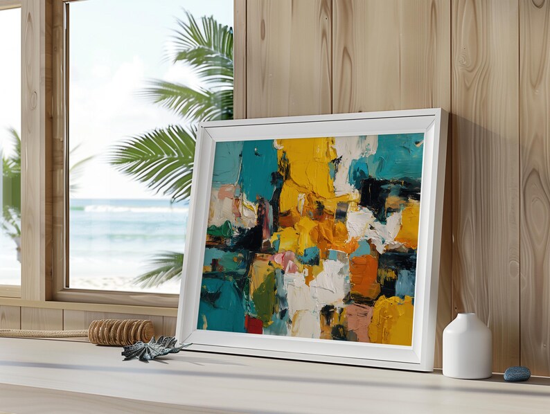 May include: A framed abstract painting with a white border. The artwork features bold brushstrokes in shades of yellow, teal, orange, white, and black. The painting is displayed on a white surface near a window with a view of the ocean.
