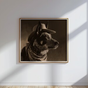 May include: Sepia-toned framed print of a dog wearing a cowboy hat and bandana. The dog is a medium-sized breed with upright ears, and the artwork has a vintage aesthetic. The print is displayed on a white wall.