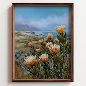 Puede incluir: Pintura de paisaje enmarcada con flores de protea de flores naranjas y blancas, sobre un fondo costero con cielo azul y mar. La obra de arte está en un marco de madera marrón oscuro.