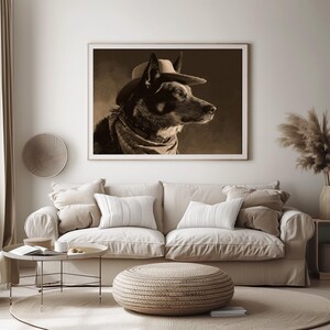 May include: Sepia-toned framed print of a dog wearing a cowboy hat and bandana. The dog is a medium-sized breed with dark fur, and the artwork is displayed above a beige sofa with decorative pillows. The room has a neutral color palette.