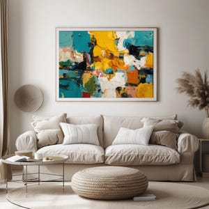May include: Abstract art painting with a wooden frame. The artwork features bold brushstrokes in shades of yellow, teal, white, and black. The painting hangs above a beige sofa with white pillows, a round woven ottoman, and a small side table.