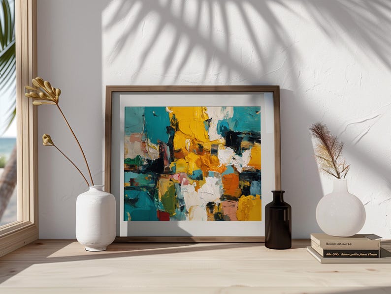 May include: Abstract art print in a wooden frame. The artwork features bold brushstrokes of yellow, teal, white, and orange. A white vase with dried flowers and a black bottle are on a wooden surface.