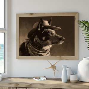 May include: Sepia-toned framed print of a dog wearing a cowboy hat and bandana. The dog is a medium-sized breed with dark fur, and the artwork is displayed on a wooden surface with decorative items.