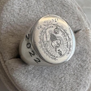 May include: A silver ring with a detailed design featuring an eagle and the year 2022 engraved on the side. The ring has a raised circular design with a wreath of stars and the text "LIBERTY" and "E PLURIBUS UNUM".