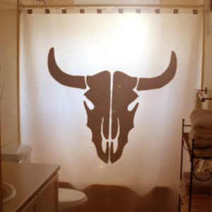May include: A white shower curtain with a black silhouette of a bull skull. The shower curtain is hung on a shower rod.