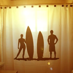 May include: Silhouettes of two people standing in front of three surfboards on a white shower curtain. The shower curtain has a light brown background.