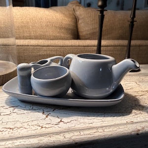 May include: A light blue ceramic tea set with a teapot, creamer, sugar bowl, and a matching tray. The set is on a white, distressed wooden surface.