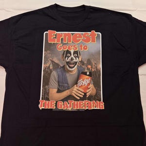 Puede incluir: Camiseta negra con un gráfico de una persona maquillada de payaso sosteniendo una botella de refresco Faygo. El gráfico dice "Ernest Goes to The Gathering" en texto rojo y blanco.