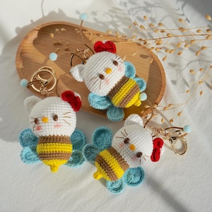 May include: Three crocheted bee keychains with white fuzzy faces, red bows, and yellow and brown striped bodies. The bees have blue wings and are attached to gold key rings.