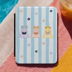 May include: A rectangular e-reader case featuring a light blue and white vertical striped pattern. The design includes three small ghost figures in lavender, peach, and yellow, each reading a book, surrounded by scattered small flower icons.