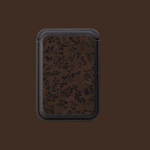 May include: A rectangular, brown leather phone case with a black border. The case features a floral pattern in a darker shade of brown. The design is a subtle, yet elegant, accessory.