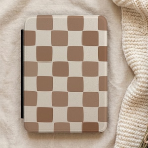 May include: A rectangular electronic reader case featuring a repeating checkered pattern of rounded squares in alternating shades of light beige and medium brown. The case has a smooth, flat surface and a thin black spine visible along the left side.