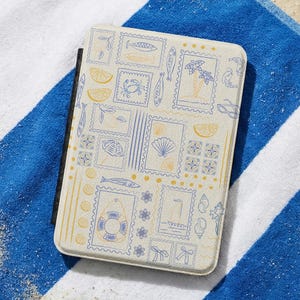 May include: A rectangular tablet case with a cream-colored surface featuring a repeating pattern of blue and yellow line-art illustrations including fish, seashells, a lifebuoy, a sailboat, palm trees, lemon slices, and small floral motifs.