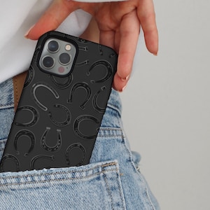 May include: Black phone case with a repeating horseshoe pattern. The case is in a pocket of blue denim jeans. The horseshoe design is a darker shade of black than the case itself.