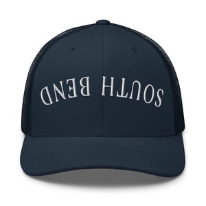 Op de afbeelding: Een marineblauwe truckerpet met een mesh achterkant en een gebogen klep. De witte geborduurde tekst "SOUTH BEND" is over de voorkant gebogen. Een klassiek, casual accessoire.