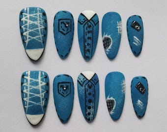 May include: A set of ten blue and white press-on nails. Designs include a sneaker, denim jacket, and a nail with the word "Luck". The nails are oval-shaped and have a matte finish.