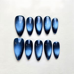 Puede incluir: Conjunto de diez u&ntilde;as postizas de ojo de gato de color azul y blanco con forma ovalada puntiaguda.