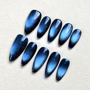 Puede incluir: Conjunto de diez u&ntilde;as postizas de color azul y plateado con efecto ojo de gato y forma ovalada puntiaguda.