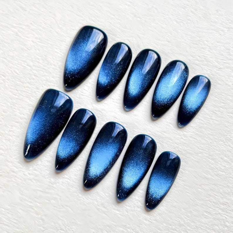 Puede incluir: Conjunto de diez u&ntilde;as postizas de color azul y plateado con efecto ojo de gato y forma ovalada puntiaguda.