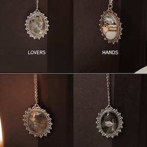 May include: Four ornate, silver-toned pendants with oval-shaped centers and delicate chain attachments. Each pendant features a different image: a cloudy stone, a couple, a tree-like pattern, and a swan. The word "LOVERS", "HANDS", "TREES", and "SWAN" are printed below each pendant.