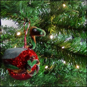 May include: A red and green Christmas ornament shaped like a dinosaur with a glittery finish.