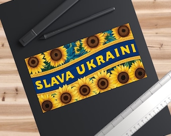 Może przedstawiać: Naklejka w kolorze niebieskim i żółtym z słonecznikami i napisem "SLAVA UKRAINI" żółtymi literami.