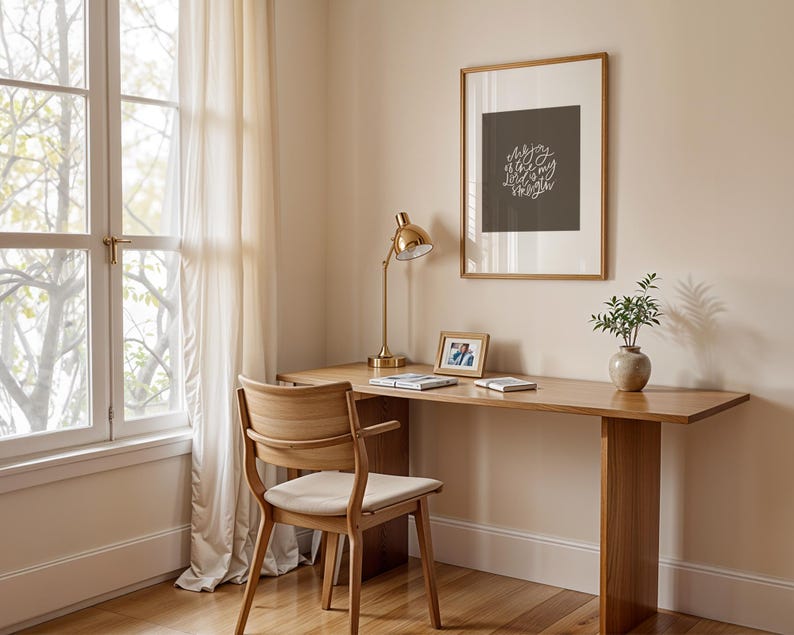 Pode incluir: Uma secret&aacute;ria de madeira clara com uma cadeira a condizer est&aacute; colocada perto de uma janela com cortinas transparentes. Uma l&acirc;mpada de secret&aacute;ria dourada, arte emoldurada com texto, uma pequena moldura e um vaso com vegeta&ccedil;&atilde;o est&atilde;o na secret&aacute;ria.