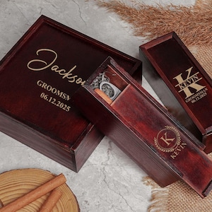 May include: Two wooden gift boxes with engraved names and dates. The larger box is labeled "Jackson GROOMSMN 06.12.2025" and the smaller box is labeled "Kevin GROOMSMAN 06.12.2025". Both boxes have a gold initial engraved on the lid.