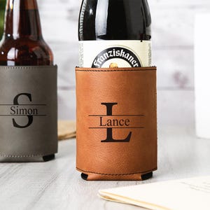 May include: Two personalized beer can coolers. One is gray with the name "Simon" and the initial "S". The other is brown with the name "Lance" and the initial "L". Both are made of a leather-like material.