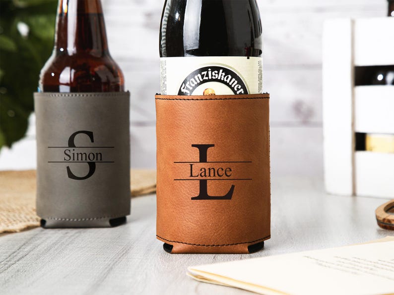 May include: Two personalized beer can coolers. One is gray with the name "Simon" and the initial "S". The other is brown with the name "Lance" and the initial "L". Both are made of a leather-like material.