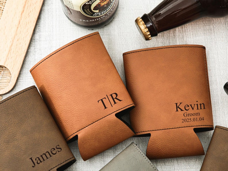 May include: A collection of personalized brown leatherette can coolers. One cooler is engraved with the initials "T|R", another with the name "Kevin", the word "Groom", and the date "2025.01.04". Other coolers are visible with names engraved.