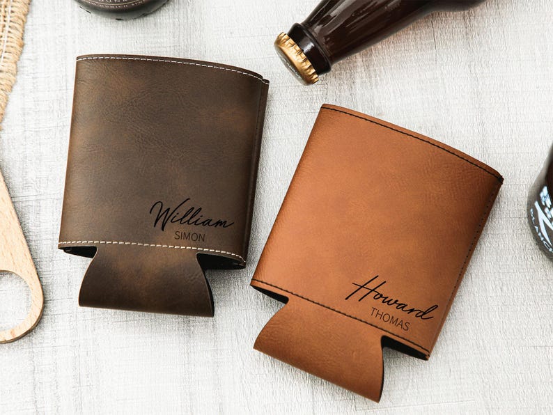 May include: Two personalized leather beer can coolers in brown and tan. The brown cooler is embossed with "William Simon" and the tan cooler has "Howard Thomas" in a script font. Both have a stitched border and a cutout for the can.