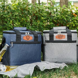 Pu&ograve; includere: Due borse frigo isolate, una blu e una grigia, con dettagli neri e toppe personalizzate in similpelle. La borsa blu ha l'iniziale "J" e il nome "James". La borsa grigia ha il nome "Jackson". Entrambe le borse hanno una maniglia superiore e una tasca frontale con cerniera.