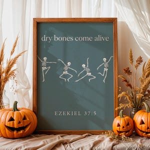 May include: A framed wall art print with a dark teal background featuring four white skeletons in various dancing poses. The text "dry bones come alive" is printed in white at the top, and "EZEKIEL 37:5" is printed in white at the bottom.