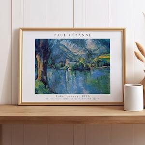 May include: A framed art print featuring Paul Cézanne's Lake Annecy, 1896. The painting depicts a blue lake, mountains, and a dark tree trunk. Text reads: PAUL CÉZANNE, Lake Annecy, 1896, The Courtauld Gallery, London, United Kingdom.