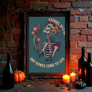 May include: A framed wall art print featuring a skeleton adorned with colorful flowers and greenery. The text "EZEKIEL 37:1-10" and "DRY BONES COME TO LIFE" is printed in a light tan font against a dark teal background within the ornate frame.