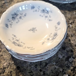 May include: A stack of four white porcelain bowls with a delicate blue floral pattern and a silver rim. The bowls have a scalloped edge and are stacked on top of each other. The floral design is repeated around the bowl's edge.