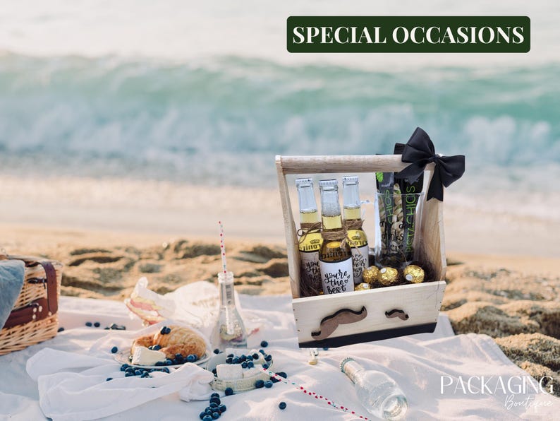 Puede incluir: Una caja de regalo de madera con un lazo negro y un dise&ntilde;o de bigote. La caja contiene tres botellas de cerveza, una bolsa de aperitivos y caramelos de chocolate. La caja est&aacute; sentada sobre una manta blanca con ar&aacute;ndanos y un pastel.