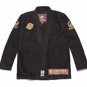 Puede incluir: Gi de Jiu-Jitsu negro con parches bordados en morado y dorado. Los parches presentan el logotipo de Shoyoroll y el texto "Shoyoroll Premium Fine Fit Jiu-Jitsu Kimonos".