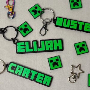 May include: Five green and black keychains with the names Elijah, Carter, Buster, and two Minecraft character charms. The keychains are made of a soft, flexible material.