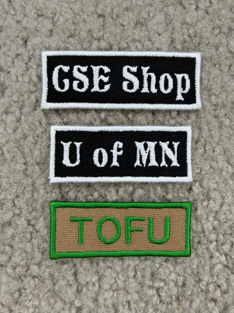 K&ouml;nnte beinhalten: Drei rechteckige, gestickte Aufn&auml;her. Der obere Aufn&auml;her ist schwarz mit wei&szlig;em Text "GSE Shop". Der mittlere Aufn&auml;her ist schwarz mit wei&szlig;em Text "U of MN". Der untere Aufn&auml;her ist beige mit gr&uuml;nem Text "TOFU".