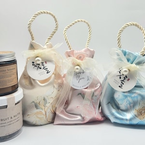 May include: An assortment of gift items, including two glass jars and three decorative bags. The jars contain "Aroma Sensation" and "Fruit & Nuts" products. The bags are in cream, pink, and blue, with floral patterns and white tags.