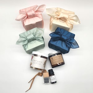 May include: An assortment of gift sets, including wrapped boxes in pink, cream, blue, and green silk fabric. Also included are jars of fruit and nuts, a candle, essential oil, and a small bottle with the text "thank you".