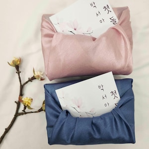 May include: Two gift boxes wrapped in fabric, one pink and one blue. Both boxes have a white card inside with Korean text that reads "Happy Birthday".