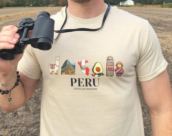 Puede incluir: Una camiseta beige con un diseño gráfico que presenta ilustraciones de símbolos peruanos, incluyendo una llama, una montaña, un mapa, un aguacate y una persona con ropa tradicional. La palabra "PERU" está impresa debajo.